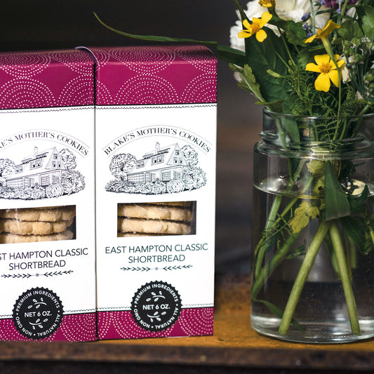 Two boxes of East Hampton Classic Shortbread sitting on a wooden table with a bouquet of country flowers.