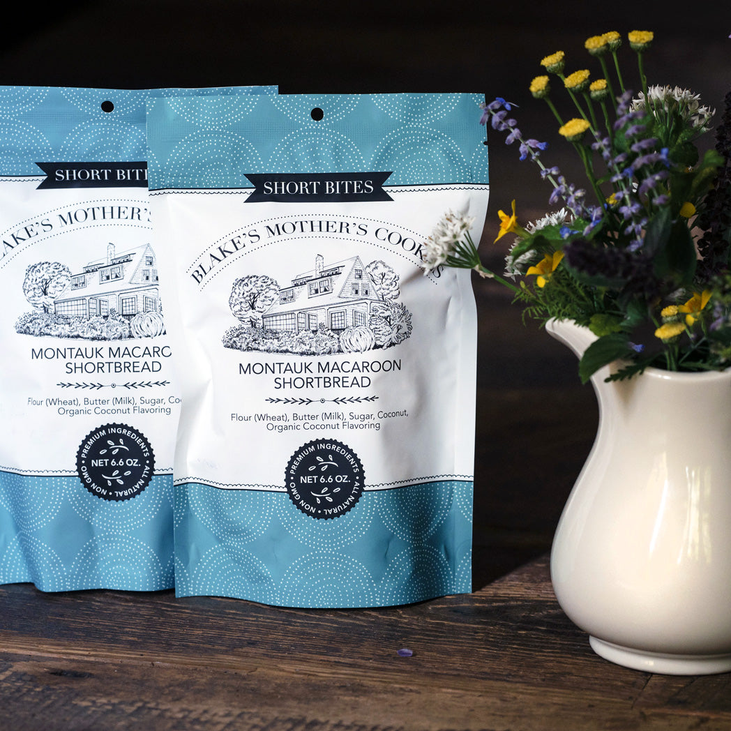 Two 6.6 oz. Blake's Mother's Cookies Shortbites Pouches sitting on a table with country flowers in an ivory vase