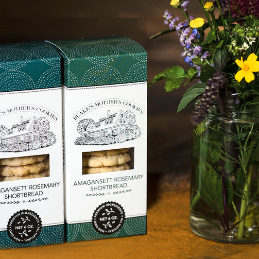 Two boxes of 6 oz. Amaganstt Rosemary Shortbread sitting on a wooden table next to country flowers