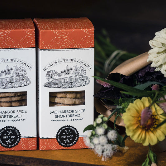 Two boxes of Sag Harbor Spice Shortbread cookies sitting on a wooden table with a country flower bouquet